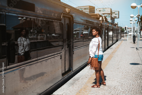 View of a beautiful mature plus-size Hispanic woman standing on a railroad platform in front of the a railway suburban train and waiting when the doors open and will be a possibility to enter it