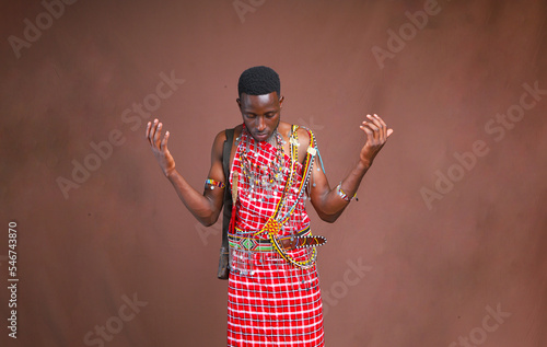 Masai moran warrior with head bowed and hands lifted praying.Huge blank brown background mockup space.Copy text and paste 
