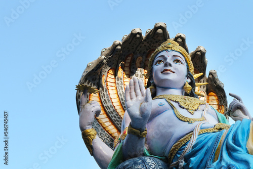 Statue of Lord Vishnu with the serpent Ananta against the blue sky.