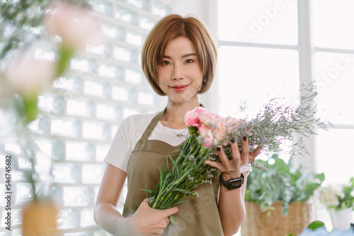 Beautiful florist Entrepreneur. Startup small business owner standing wearing apron in flower shop. Happy Asian woman holding flower and looking at camera. Flower shops,local,small businesses concept.