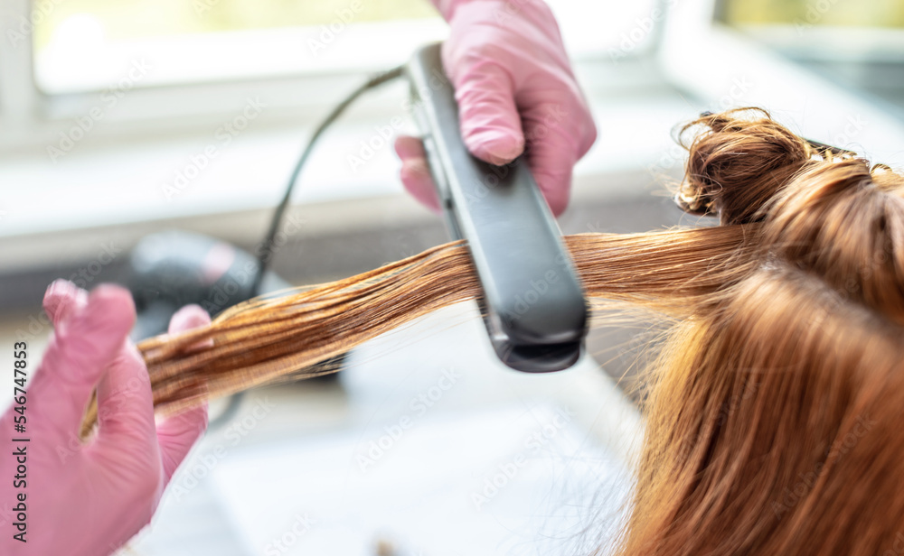 Fototapeta premium Master is running a iron through the client's hair for keratin straightening. Process of hair care procedures in the salon or at home