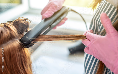 Master is running a iron through the client's hair for keratin straightening. Process of hair care procedures in the salon or at home