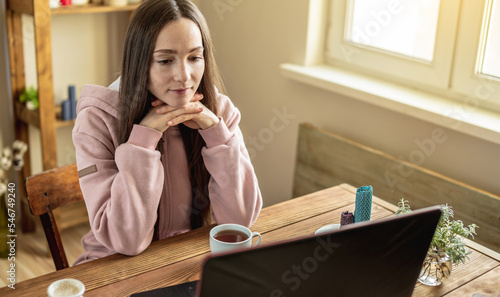 Woman is sitting in front of a computer screen in a calm pleasant atmosphere and attentively listens to video training or attends an online session with a mentor or just communicates with a friend