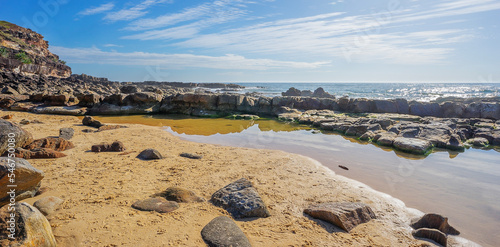 Pool of salt water on the rocky Headland at Point Arkwright with cloudy sky and a sunlit ocean.