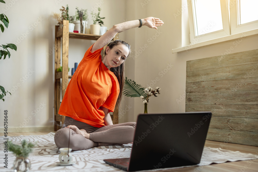 Woman in a bright clothes on the floor in front of a laptop is doing yoga using a video lesson Woman in a bright clothes on the floor in front of a laptop is doing yoga using a video lesson
