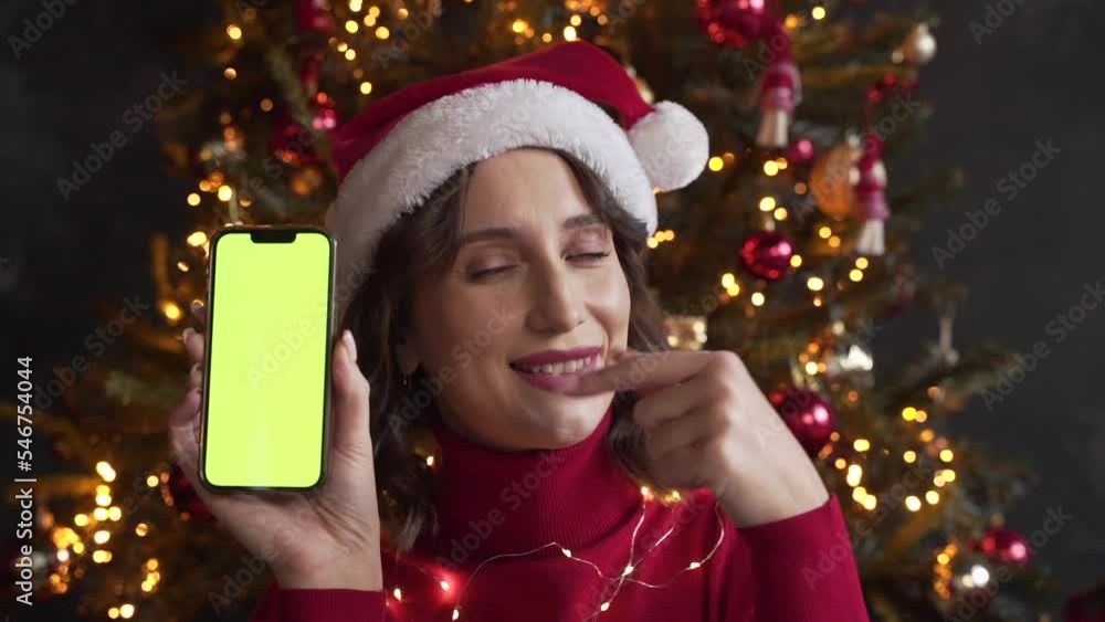 Woman in red sweater and Santa's hat holding a mobile phone with a green screen Woman in red sweater and Santa's hat holding a mobile phone with a green screen