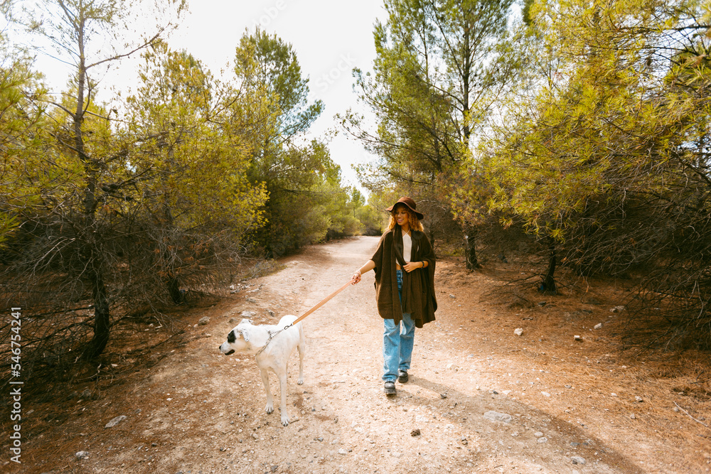 Girl with hat and poncho walking her dog smiling outdoor in sunlight Girl with hat and poncho walking her dog smiling outdoor in sunlight