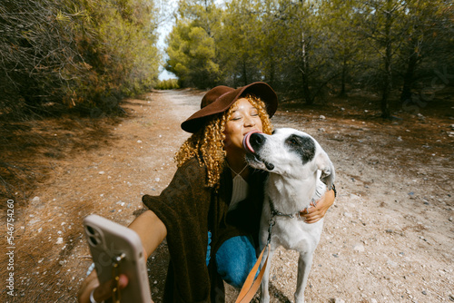 Girl with hat taking a funny selfie with her dog outdoor in sunlight photo