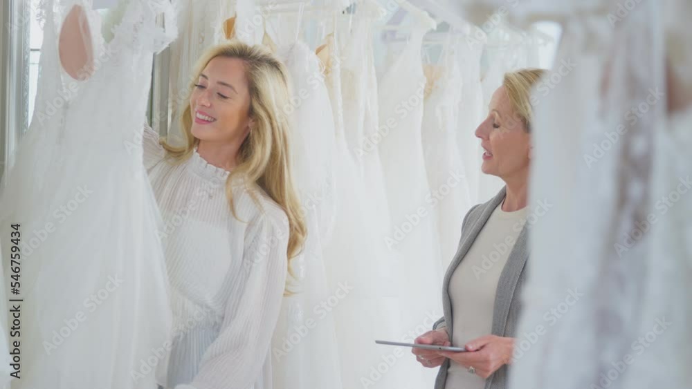 Sales assistant or shop owner with digital tablet helping woman in bridal store to choose wedding dress - shot in slow motion Sales assistant or shop owner with digital tablet helping woman in bridal store to choose wedding dress - shot in slow motion