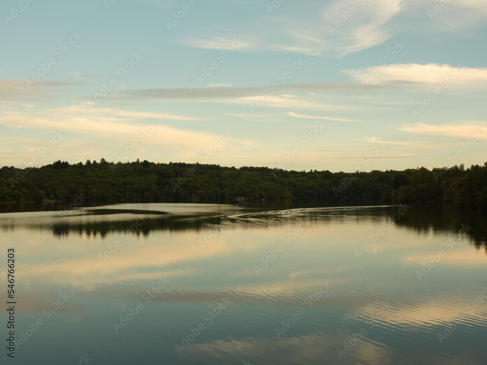 Serene sunset view of lake with reflection of blue sky and clouds Serene sunset view of lake with reflection of blue sky and clouds