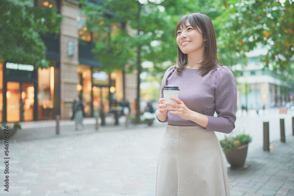 コーヒーカップを持って街を歩く女性