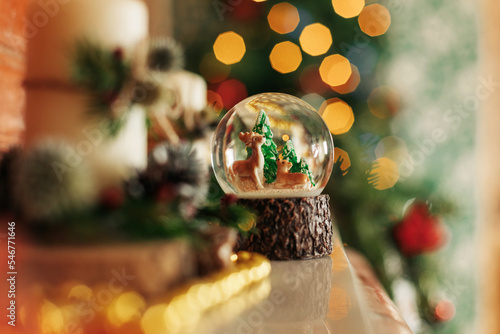 A snow globe with a snowy forest and deer stands on a shelf or fireplace. Christmas decorations, Christmas background