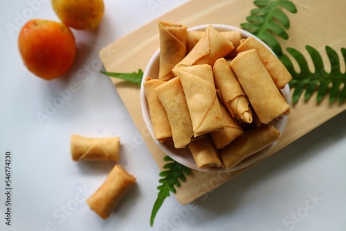 Sumpia or mini crunchy spring rolls on white plate and wooden cutting board. Indonesian homemade crispy fried snack, Wrapped by Kulit Lumpia and filled with Ebi or Shredded Shrimp. photo