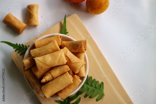 Fototapeta Naklejka Na Ścianę i Meble -  Sumpia or mini crunchy spring rolls on white plate and wooden cutting board. Indonesian homemade crispy fried snack, Wrapped by Kulit Lumpia and filled with Ebi or Shredded Shrimp.