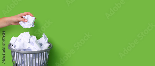 Cuadro en lienzo Woman throwing crumpled paper into trash bin on green background with space for