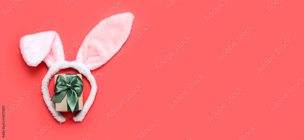 Bunny ears and Christmas gift on red background with space for text