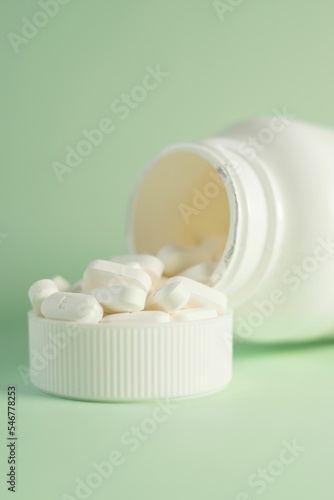 Medicine bottle and a cap filled with pills on green background - concept of health and treatment