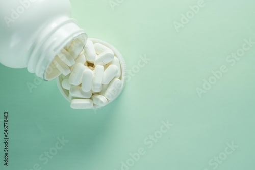 Medicine bottle and a cap filled with pills on green background - concept of health and treatment