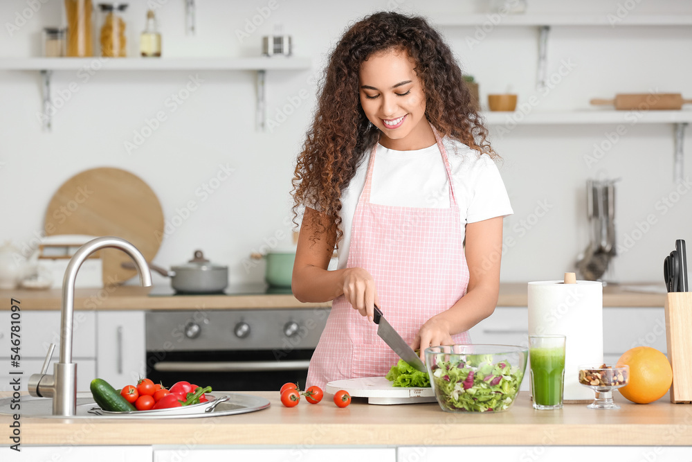 Young African-American woman making fresh salad in kitchen