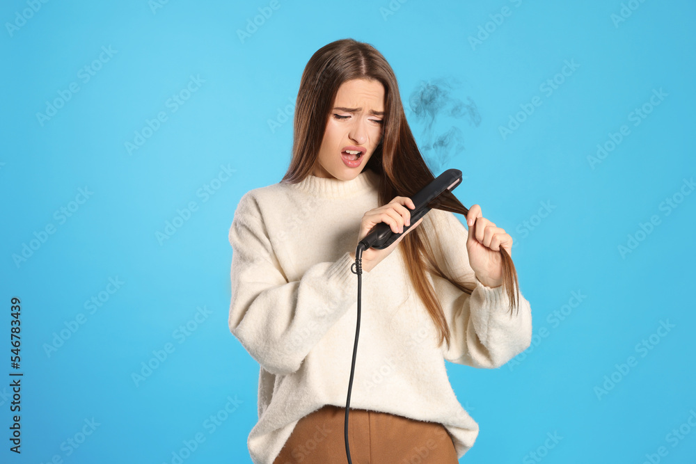 Stressed young woman with flattening iron on light blue background. Hair damage Stressed young woman with flattening iron on light blue background. Hair damage