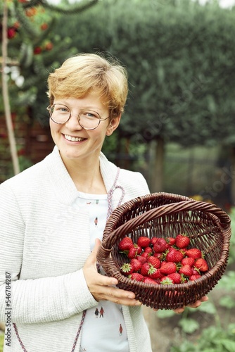 Lovely smiling kind woman with short blonde hair holding a basket of strawberries in her garden
