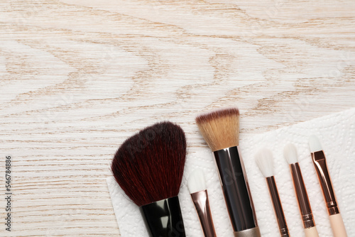 Clean makeup brushes with napkin on wooden table, flat lay. Space for text