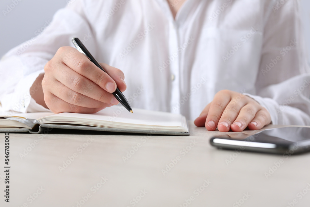 Woman writing in notebook at wooden table in office, closeup Woman writing in notebook at wooden table in office, closeup