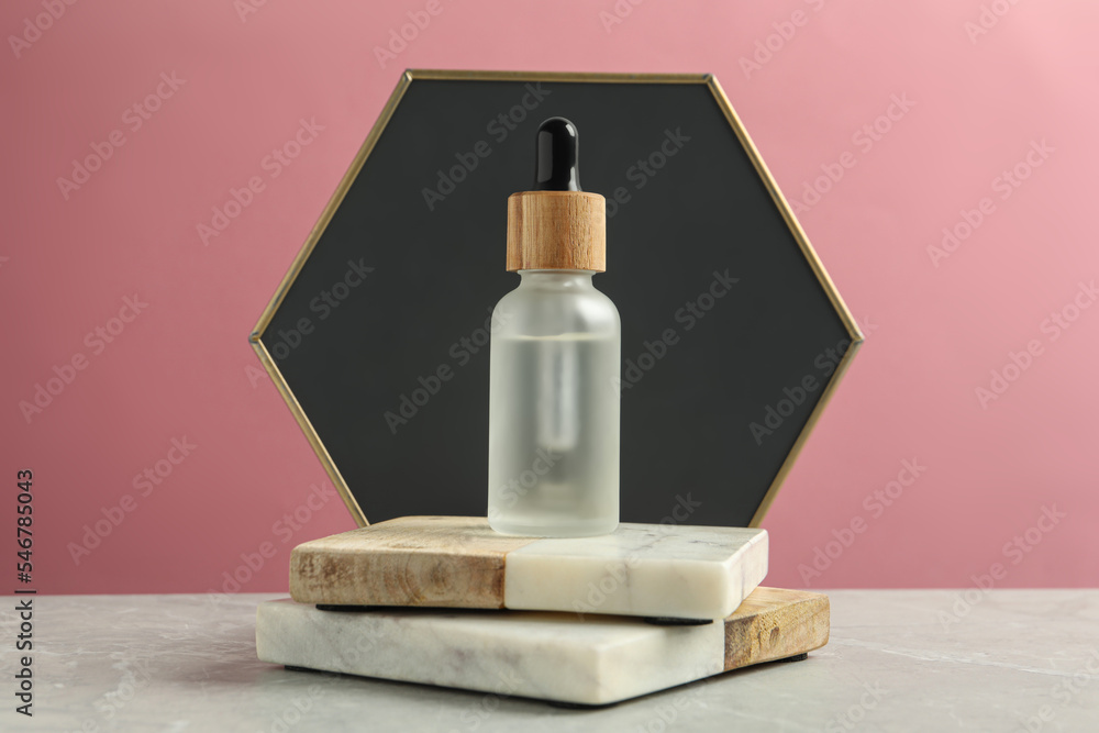 Bottle of face serum with marble boards on grey table against pink background Bottle of face serum with marble boards on grey table against pink background