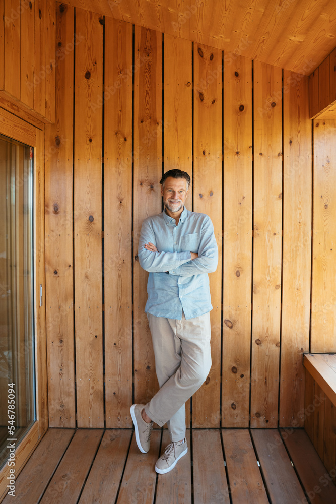 Content man standing on wooden terrace with folded arms Content man standing on wooden terrace with folded arms
