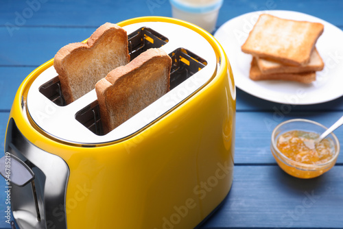 Yellow toaster with roasted bread and jam on blue wooden table, closeup