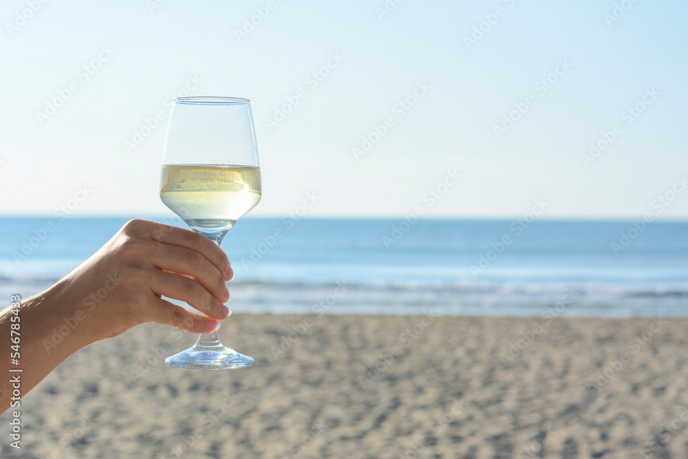 Woman with glass of tasty wine near sea, closeup. Space for text