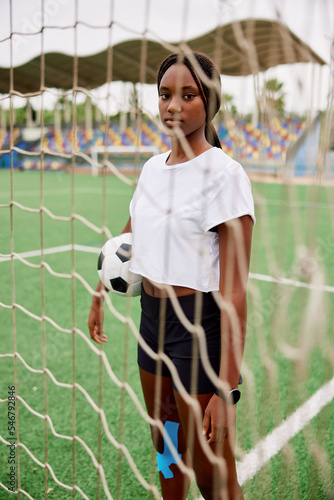 Teen black girl with ball standing near goal on field photo