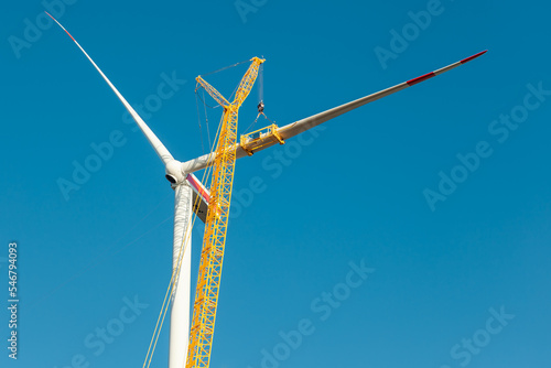 Construction work of wind turbine. crane is holding, grabbing a blade of a wind turbine. Building and assembling a wind turbine. Green energy, ecology and CO2-footprint reduction concept. Wörrstadt  © ImageSine