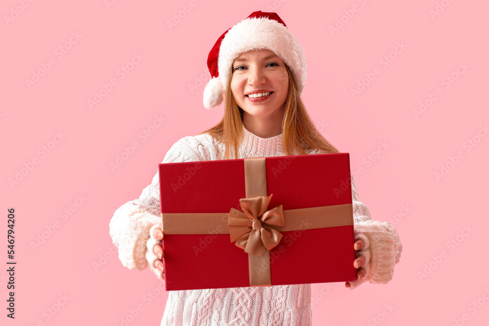 Young woman in Santa hat with Christmas present on pink background Young woman in Santa hat with Christmas present on pink background