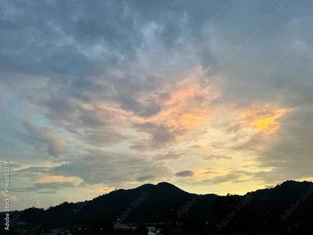 Beautiful landscape. Peak of mountains and bright sunset. Rare houses on the hillside. Amazing colorful clouds illuminated with glow of setting sun. Summer nature. Twilight in the countryside. Rural 