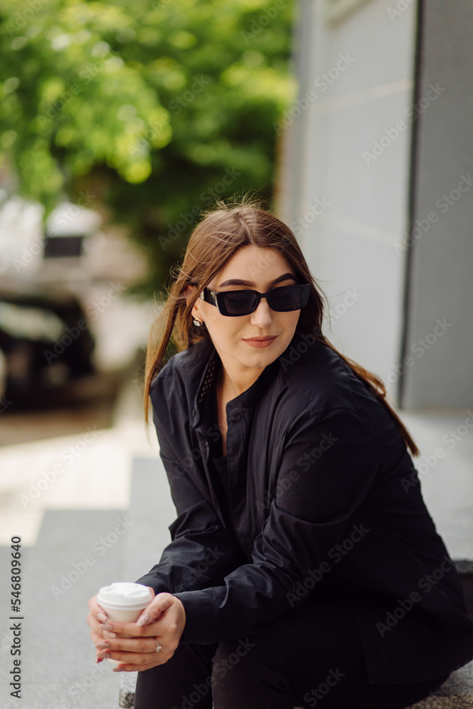 Outdoors lifestyle portrait of stunning brunette girl. Drinking coffee and walking on the city street.