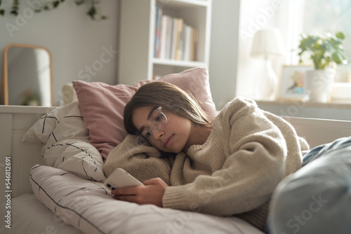 Caucasian teenage girl browsing phone while lying on bed