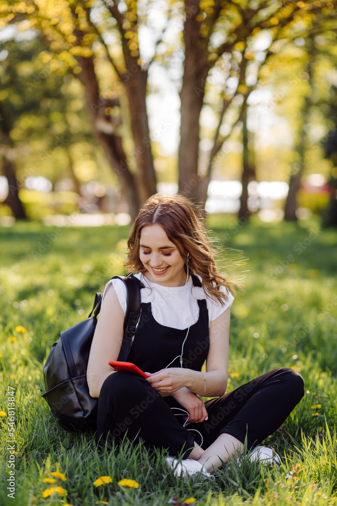 Photo of a positive cheerful teenage girl spends time in the park and using mobile phone. Photo of a positive cheerful teenage girl spends time in the park and using mobile phone.