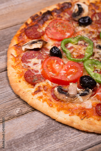 Pepperoni pizza with olives, mushrooms and green peppers, on old wood background. 