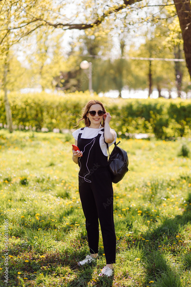 Photo of a positive cheerful teenage girl spends time in the park and using mobile phone. Photo of a positive cheerful teenage girl spends time in the park and using mobile phone.