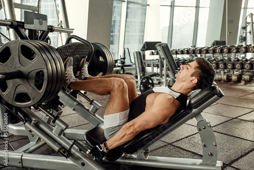 Man Using A Press Machine In A Fitness Club. Strong man doing an exercise on its feet in the simulator. Side view.