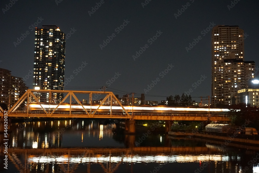 大川に架かる鉄橋に電車が通り、ビル郡の光が川に反射している夜景