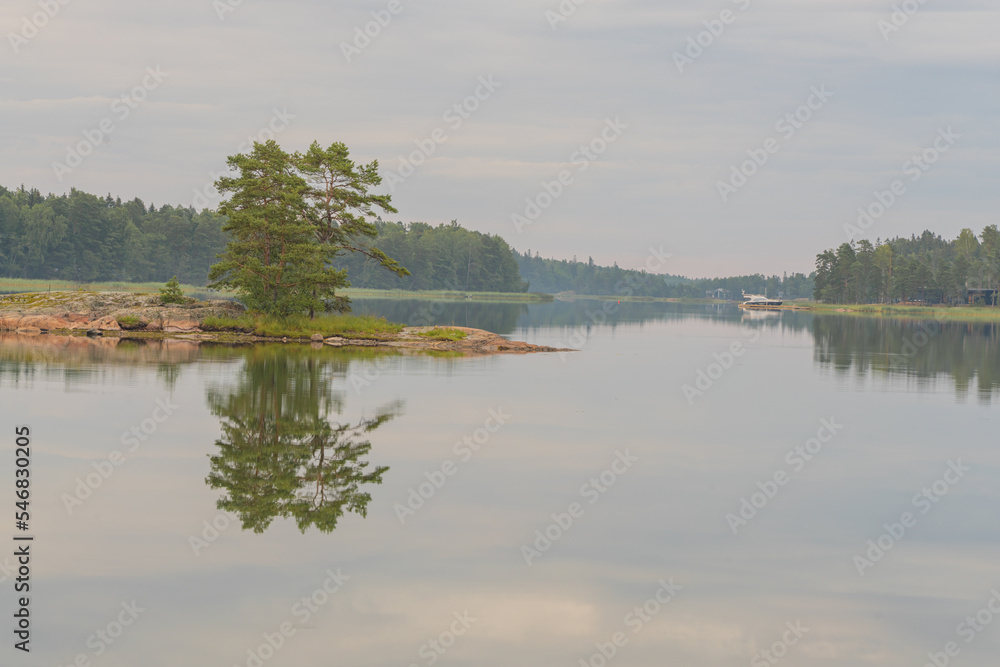 A small rocky island in the middle of a lake on a cloudy day. A small boat near the shore in the background. Autumn landscape. Natural background.
