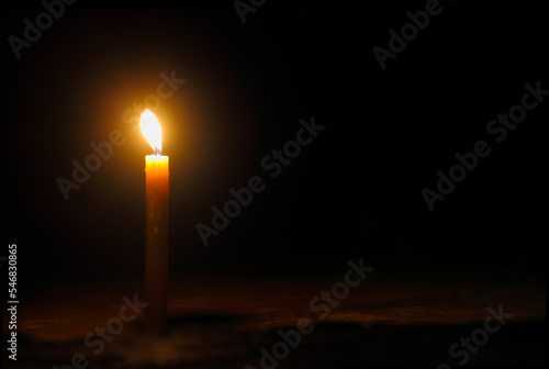 Light for a better life -One yellow candle on floor burns against the black background with copy space.