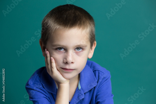 Portrait of a child, a little boy in front of a green background, a thinking expression