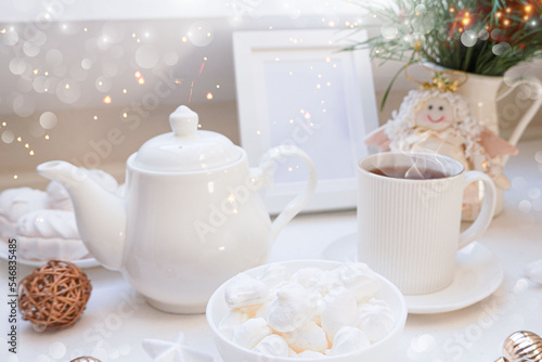  Winter  Christmas  New Year decoration composition  concept  background. White Mug  cup of hot tea  coffee  meringue  knitted plaid. Christmas lights. Christmas mood morning. Xmas greeting card.