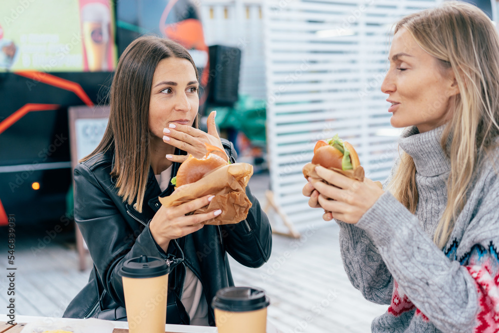 Two European women eat burgers at a food truck street fair.