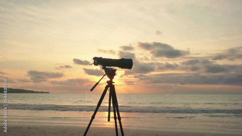 Professional camera and long lens is on a tripod on the seashore against a beautiful sunset at beach. 4K Professional camera and long lens is on a tripod on the seashore against a beautiful sunset at beach. 4K