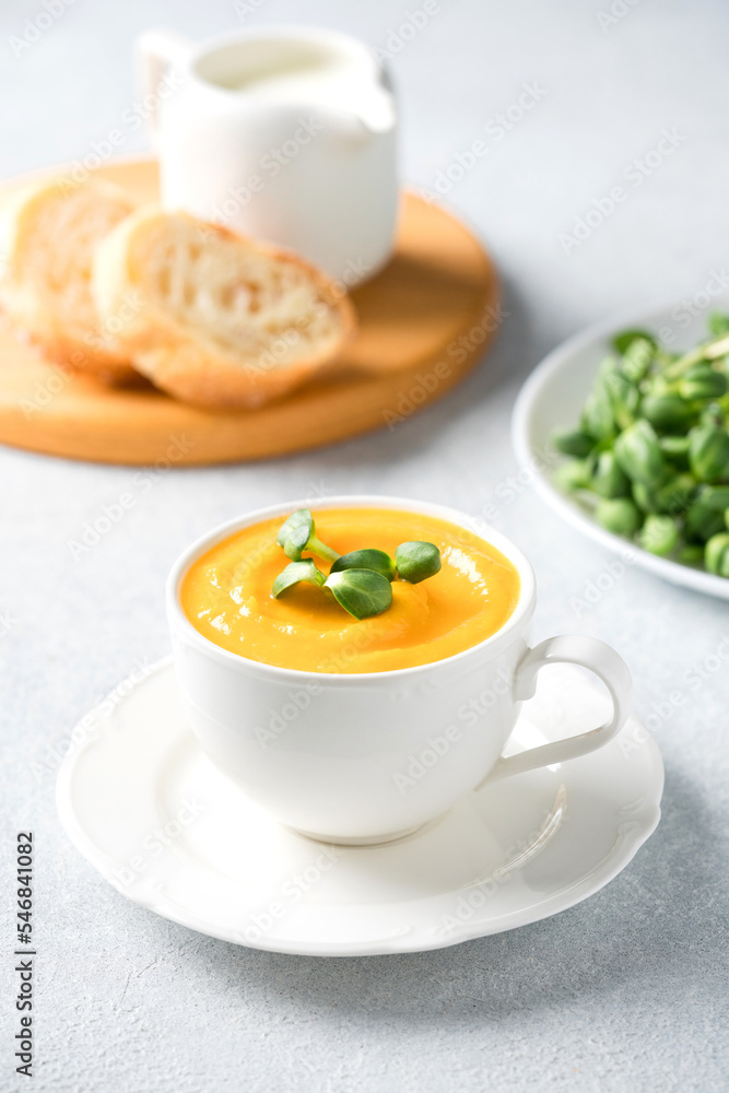 Creamy butternut squash fall soup in elegant white tea cup.Cup of pumpkin cream soup garnished with fresh sunflower microgreen. Front view, selective focus. Vertical image Creamy butternut squash fall soup in elegant white tea cup.Cup of pumpkin cream soup garnished with fresh sunflower microgreen. Front view, selective focus. Vertical image