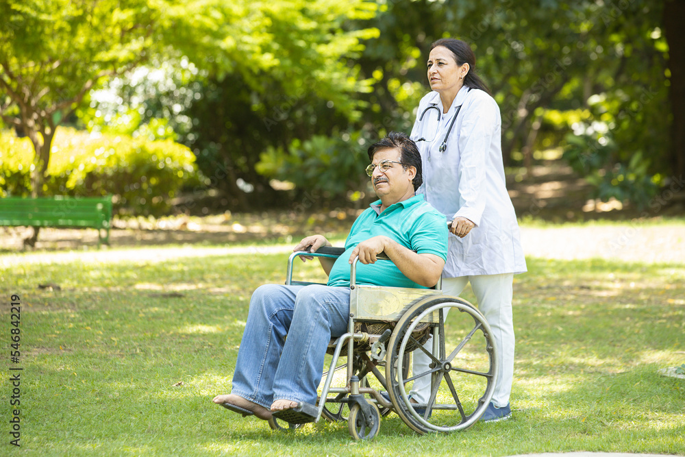 Indian caregiver nurse taking care of senior male patient in a wheelchair outdoor at park, Asian doctor help and support elderly mature older people. rehabilitation and health care. Indian caregiver nurse taking care of senior male patient in a wheelchair outdoor at park, Asian doctor help and support elderly mature older people. rehabilitation and health care.